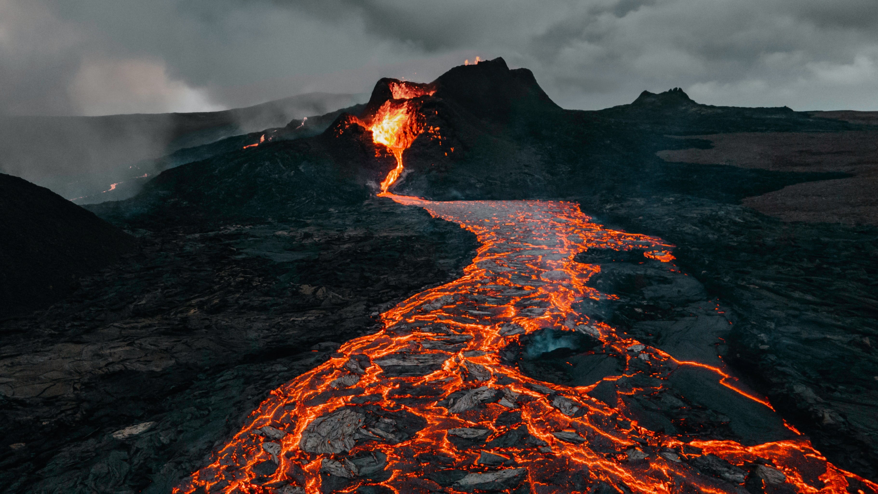 Lava flowing through a landscape with dark mountains and cloudy sky